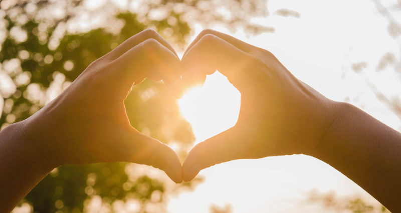 hands forming a heart shape framing the sun