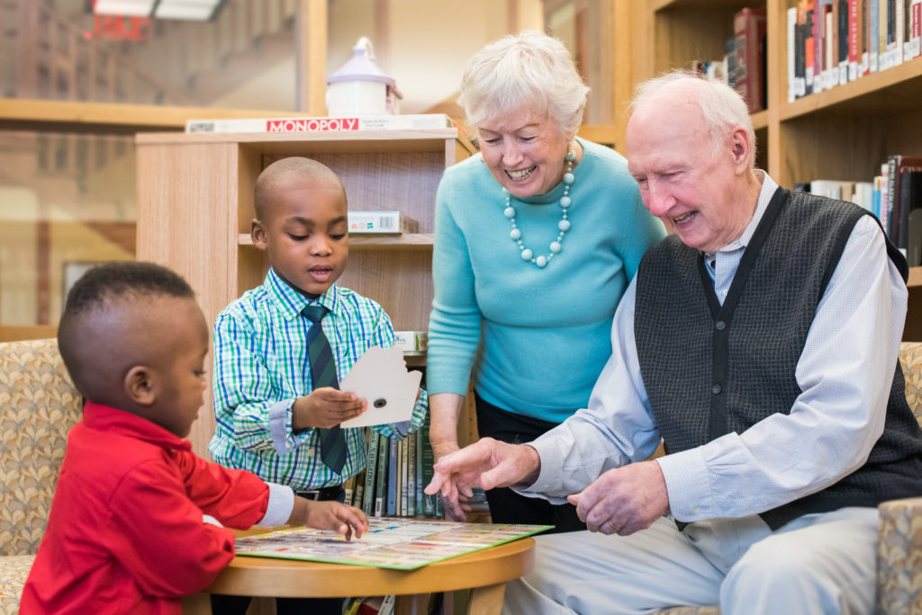Resident couple playing a game with small children in the library at Kendal on Hudson