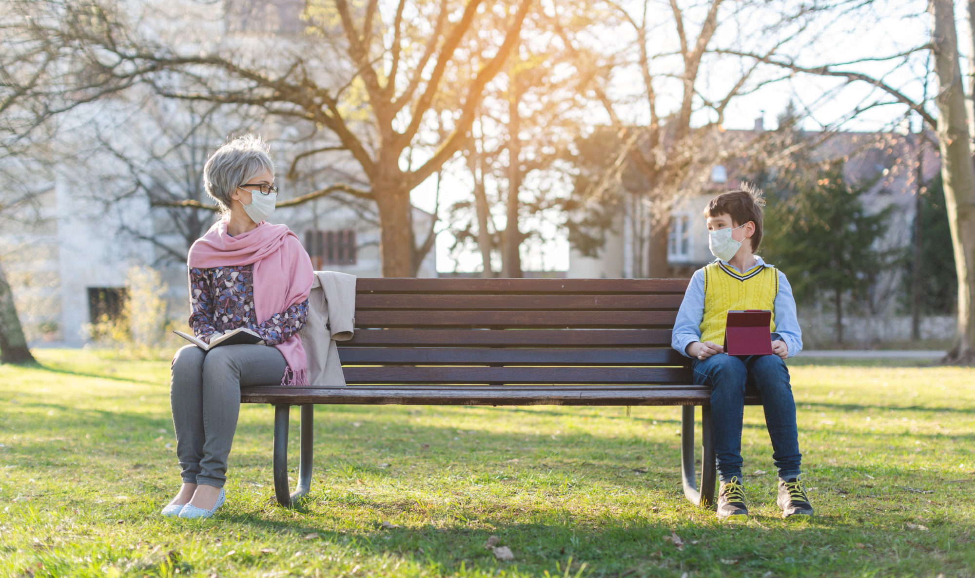 Masked senior woman and masked child sitting at a social distance from each other