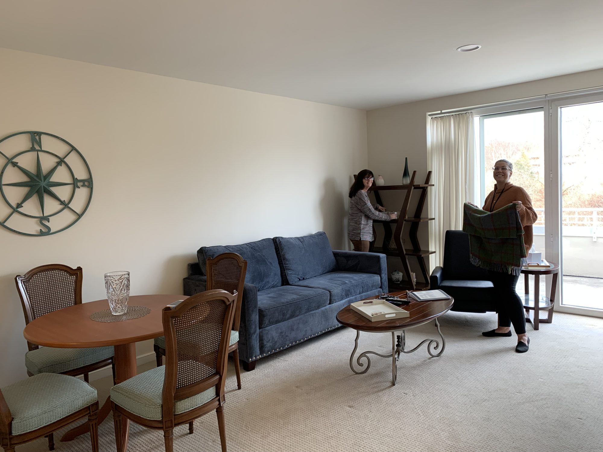 Two women smiling while organizing a living room at senior living community