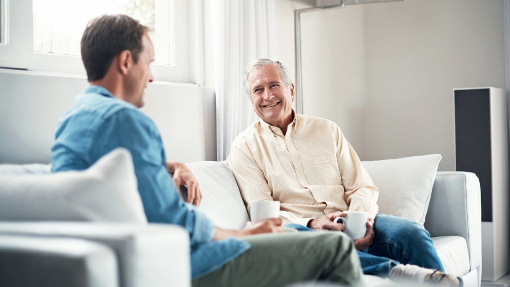 Shot of a young man and his elderly father having a chat over coffee on the sofa at home