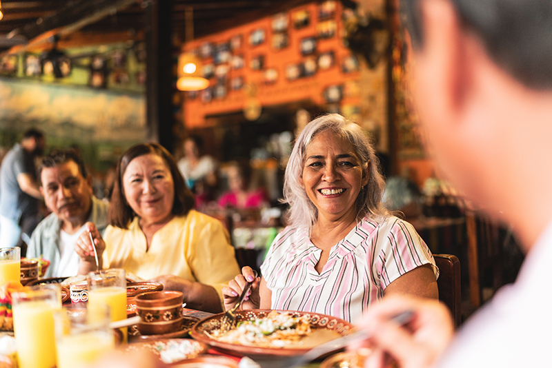 Happy senior friends talking and eating at restaurant