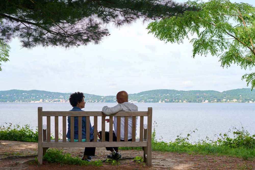 a senior couple sitting on a bench overlooking lake hudson