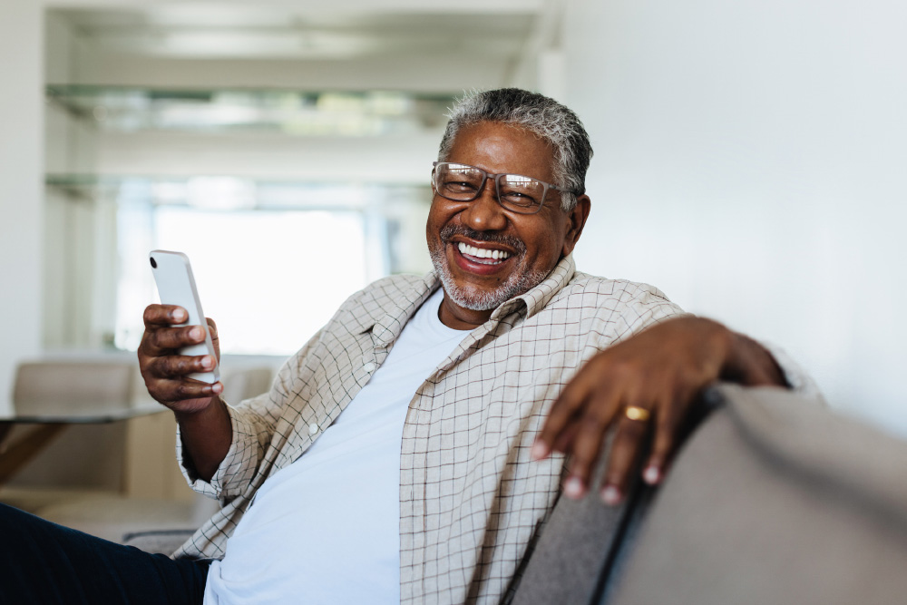 Senior sitting comfortably on the couch and smiling while holding a smartphone